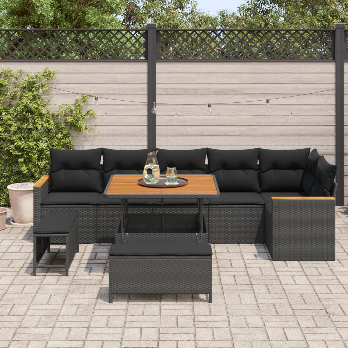 Dunkelgraue Rattan-Lounge mit Holztisch, Krügen und Glas auf gepflastertem Hof.