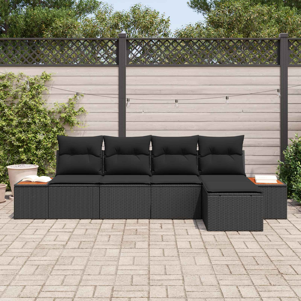 Ein schwarzes modulares Outdoor-Sofa mit Kissen steht auf einer gepflasterten Terrasse.