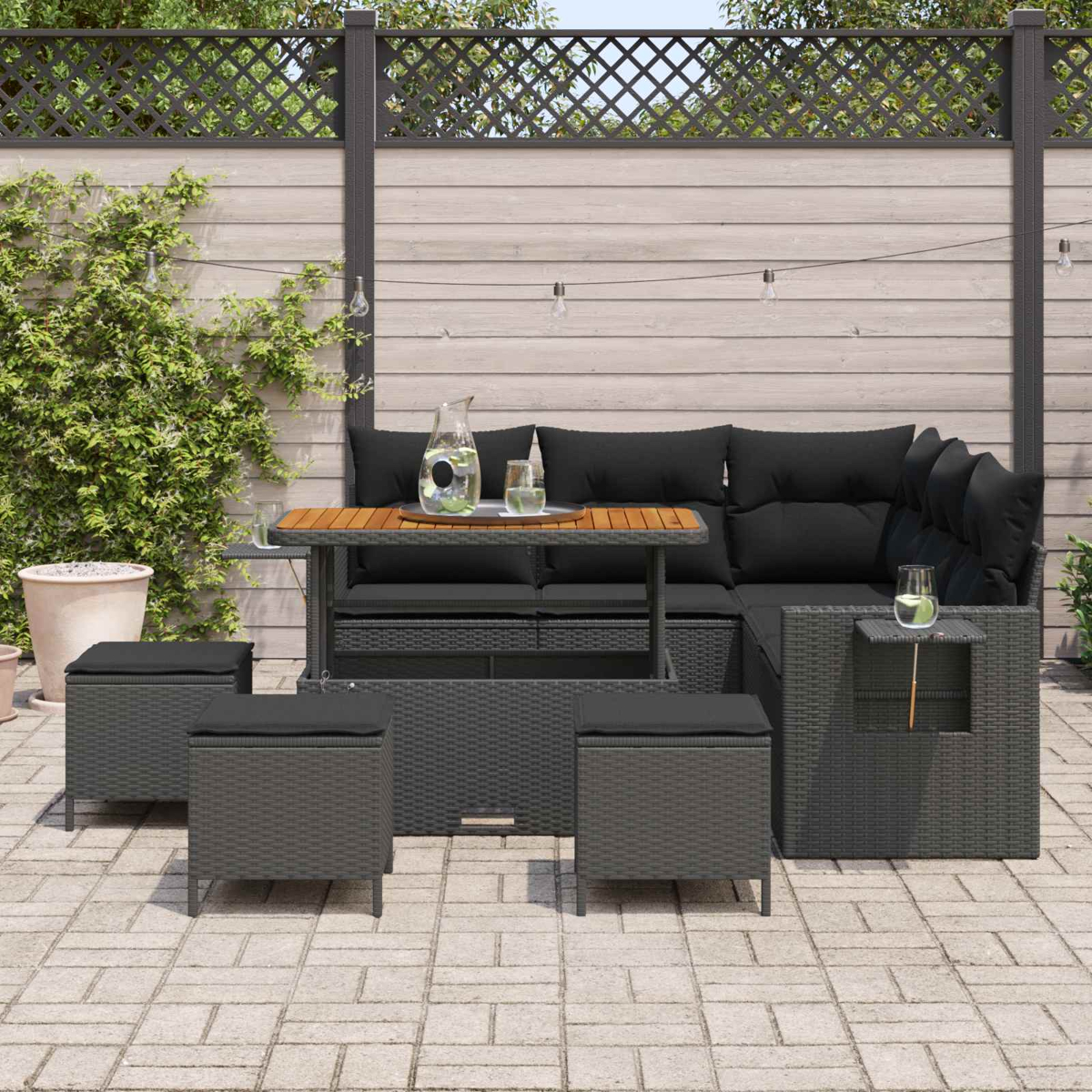 Graues Rattan-Sofa mit schwarzen Kissen, Tisch und Hockern auf einer Terrasse.