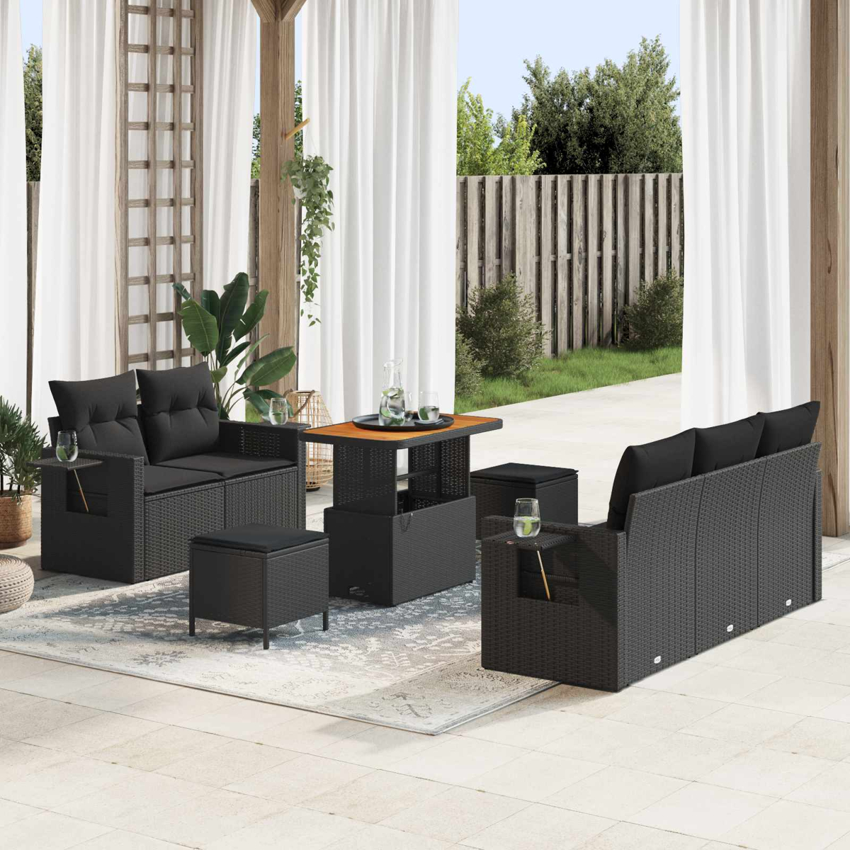 Schwarzes Rattan-Möbelset mit Sofa, Stühlen, Hocker und Tisch auf einer Terrasse.