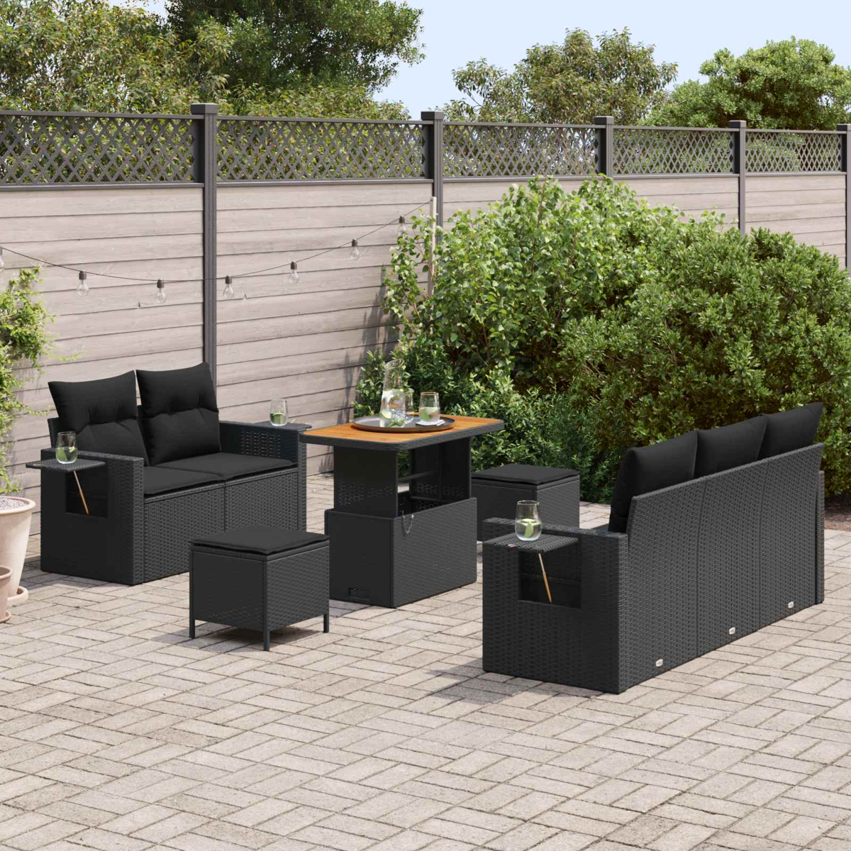 Dunkles Rattan-Gartenmöbel-Set mit Sofas, Hockern und Tisch auf einer gepflasterten Terrasse.