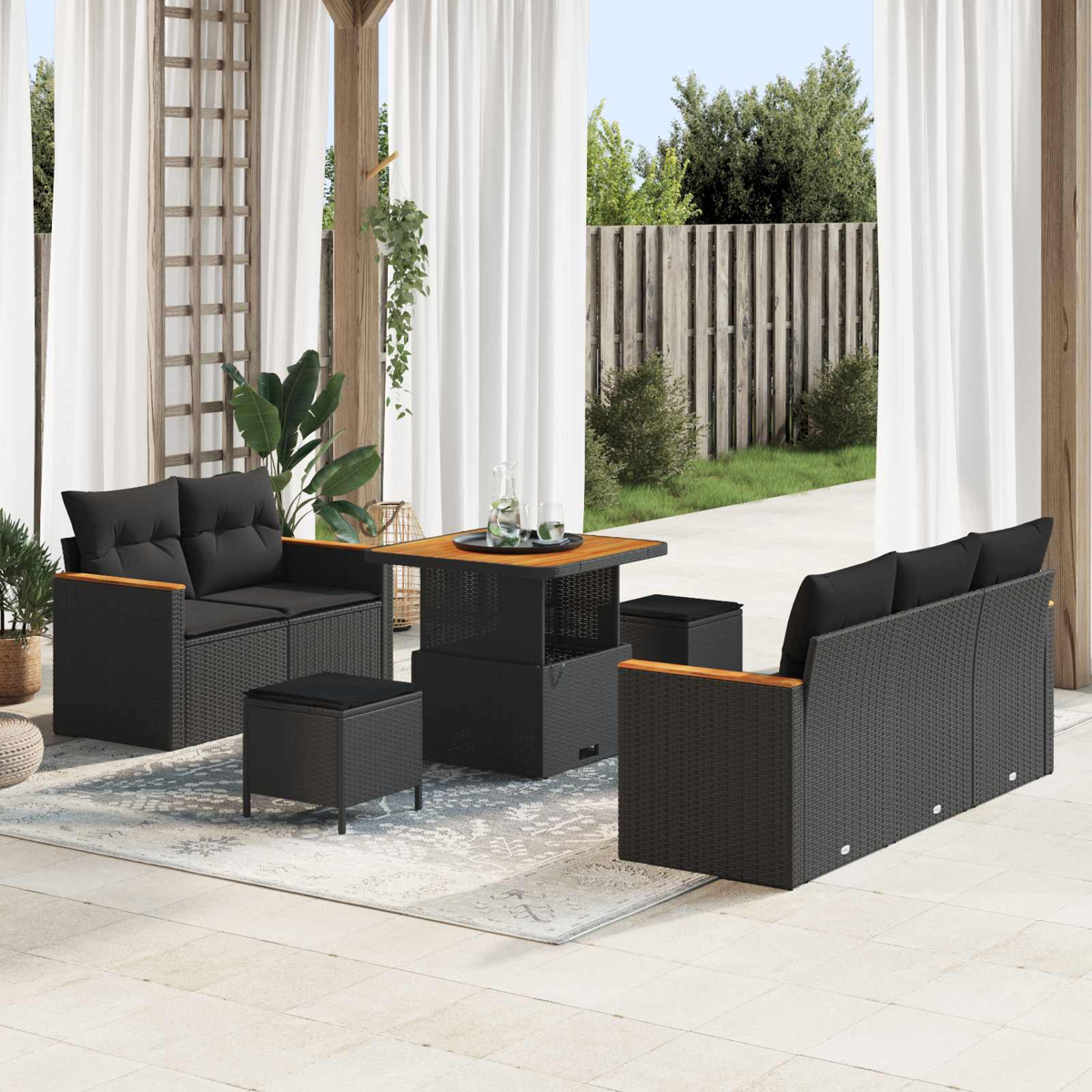 Schwarzes Rattan-Möbelset mit Kissen auf einer Terrasse mit Holzzaun und Grünpflanzen.