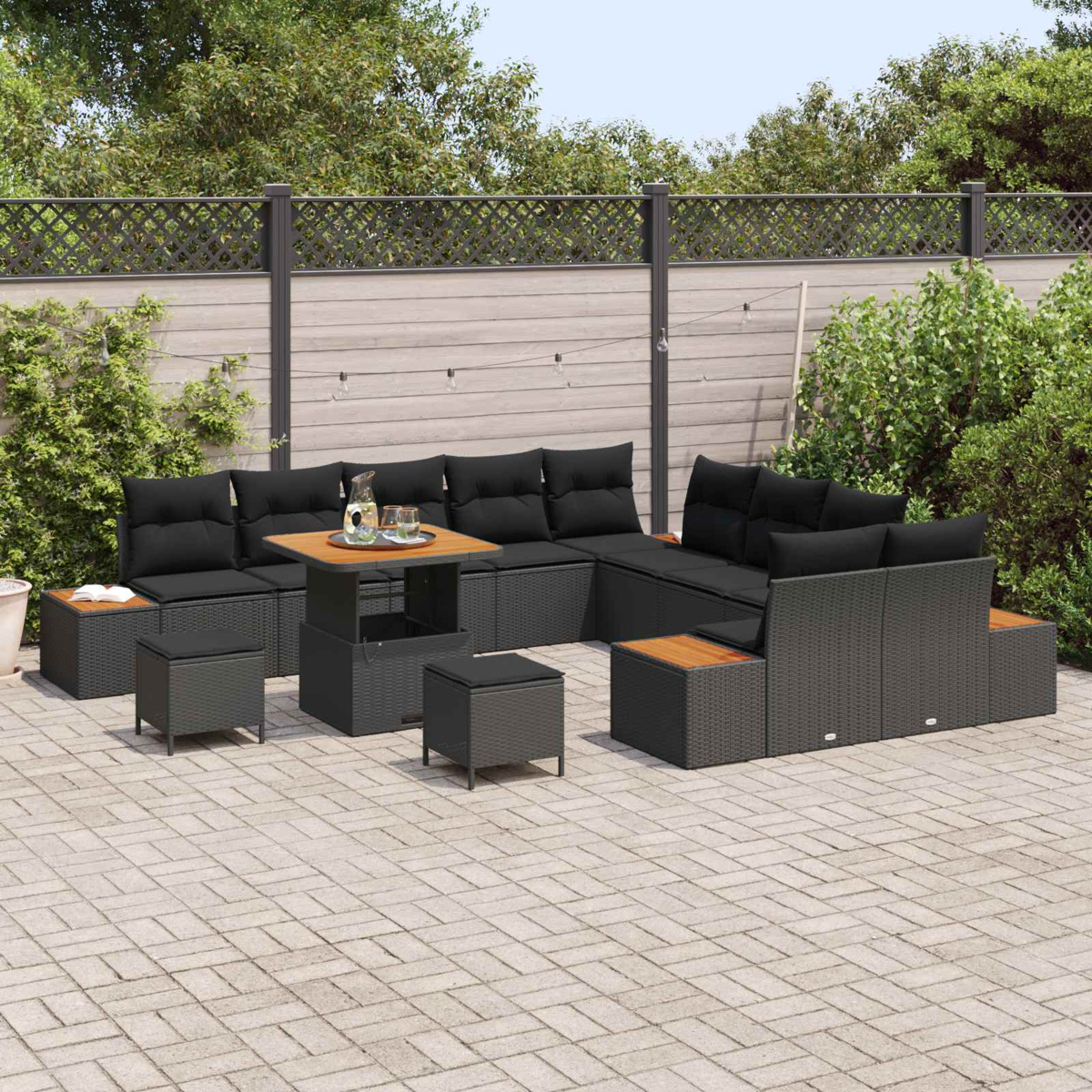 Ein dunkles Gartenmöbel-Set mit schwarzen Kissen auf einer gepflasterten Terrasse.