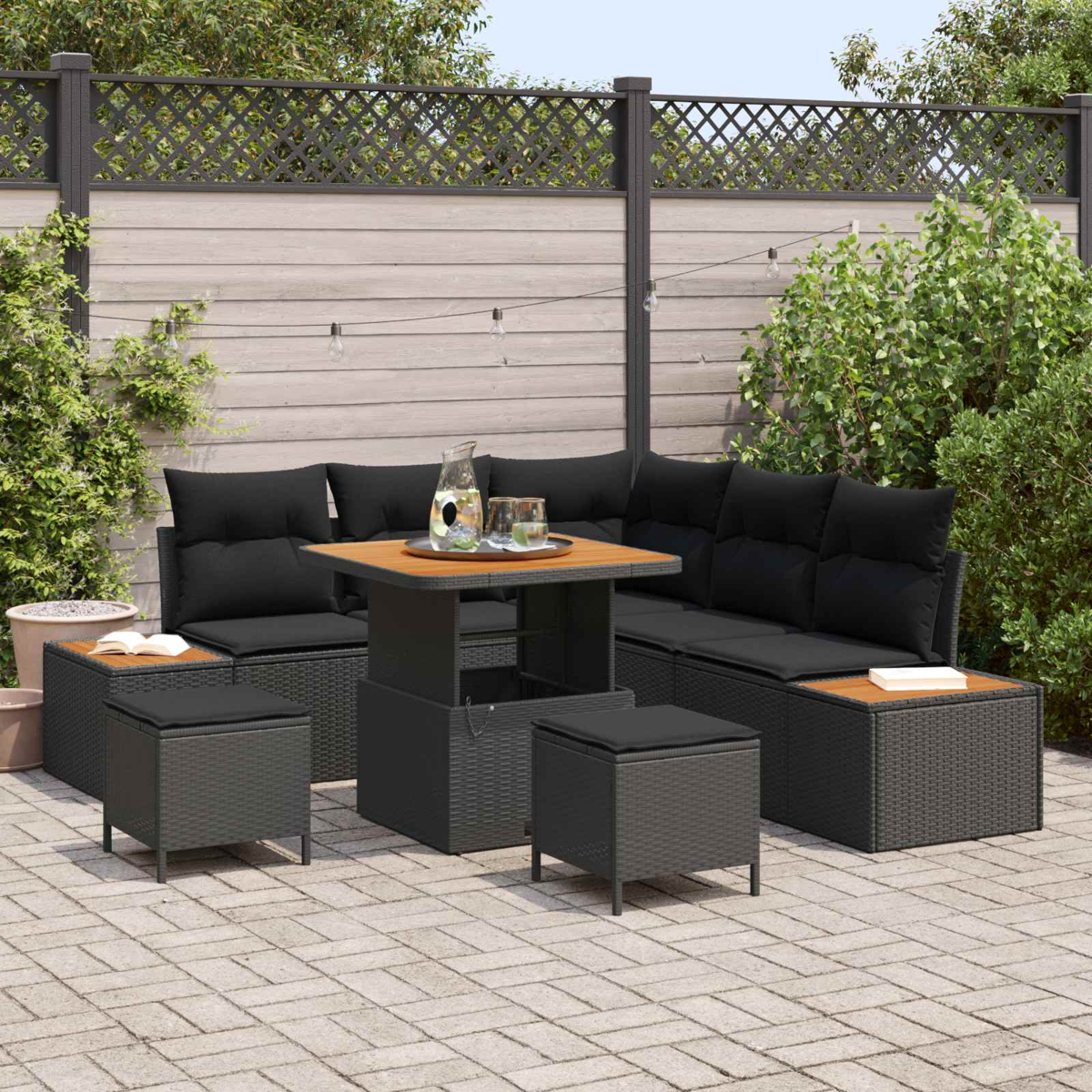Ein moderner Gartenloungetisch mit schwarzen Kissen und Hockern auf einer Steinterrasse.