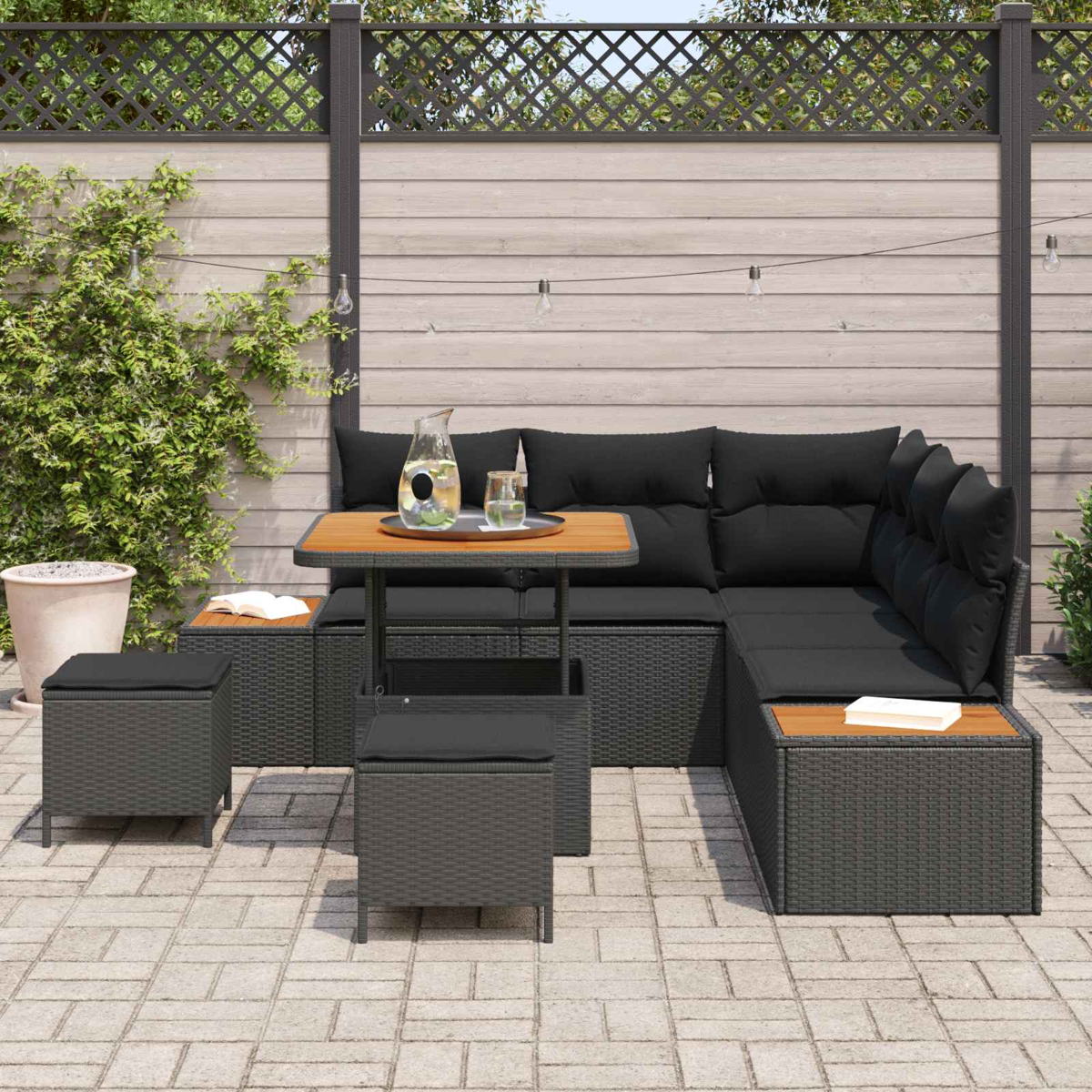 Ein dunkles Rattan-Gartenmöbelset mit schwarzen Kissen auf einer gepflasterten Terrasse.
