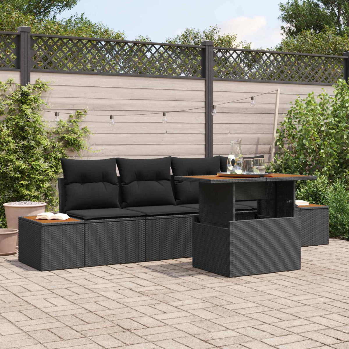 Ein dunkles Rattansofa mit schwarzen Kissen steht auf einer Steinterrasse neben einem Tisch.