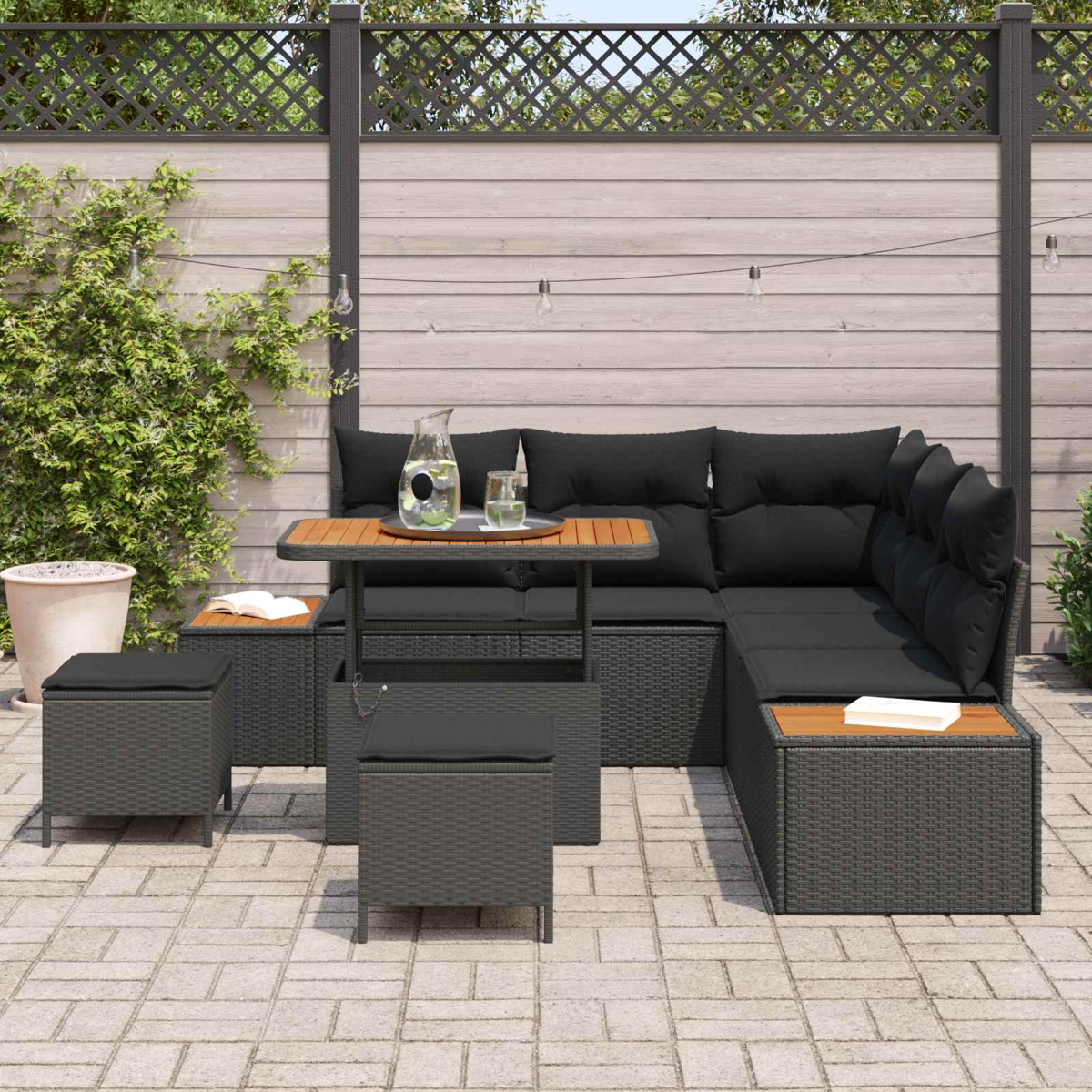 Gartensitzgruppe mit dunklen Polstern, Tisch und Hockern auf gepflasterter Terrasse.