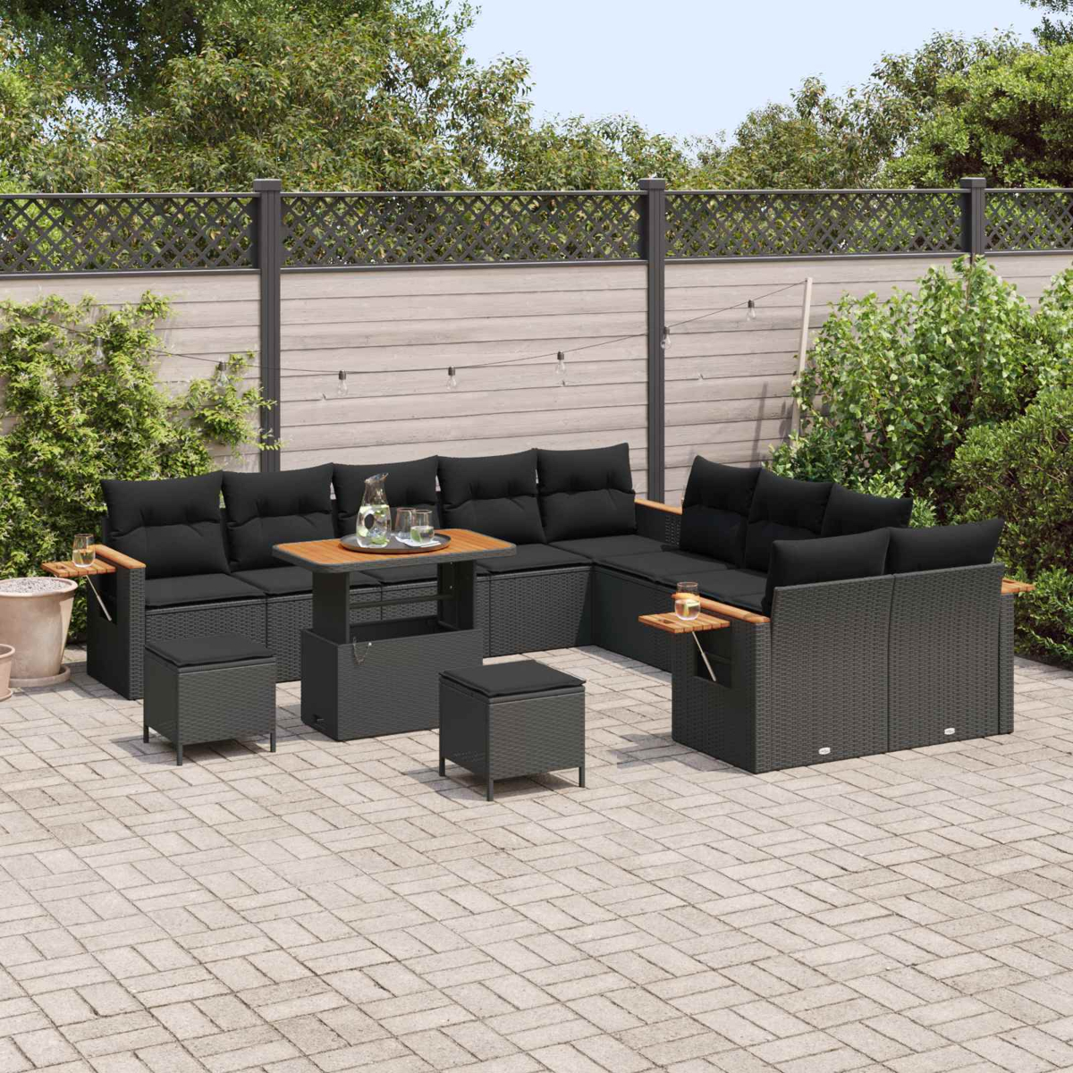 Ein dunkles Lounge-Set aus Rattan mit schwarzen Kissen auf einer gepflasterten Terrasse.