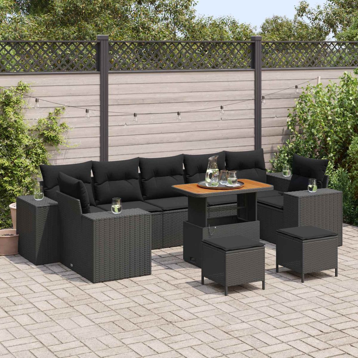 Dunkelgraue Rattan-Lounge-Möbel mit schwarzen Kissen auf einer Pflastersteinterrasse.