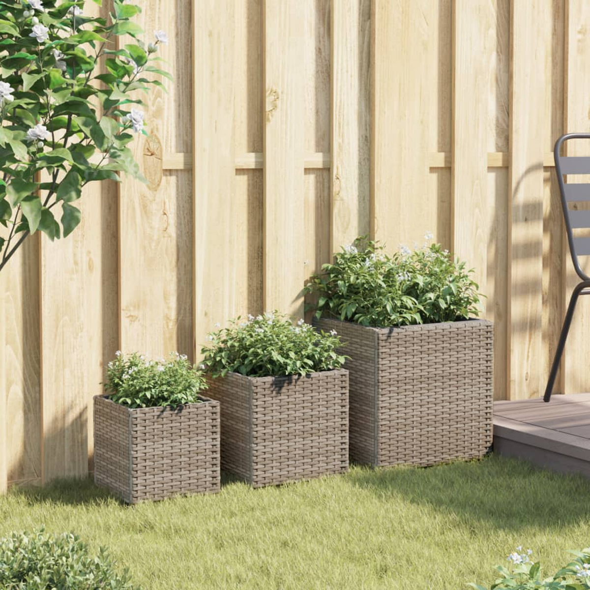 Tre fioriere rettangolari effetto rattan sull'erba davanti a una staccionata in legno.