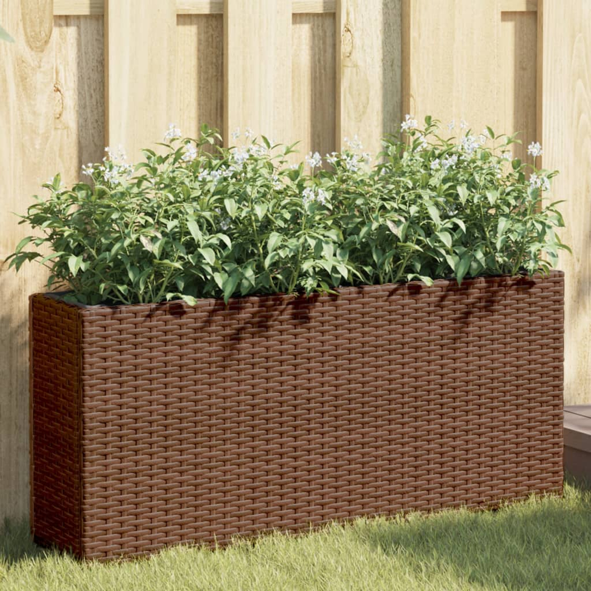Una fioriera rettangolare in rattan marrone con piante verdi e fiori bianchi.