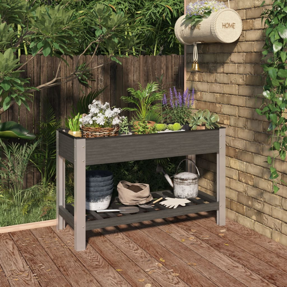 Ein Hochbeet mit Pflanzen, Werkzeugen und Bewässerungskanne auf einer Holzterrasse.