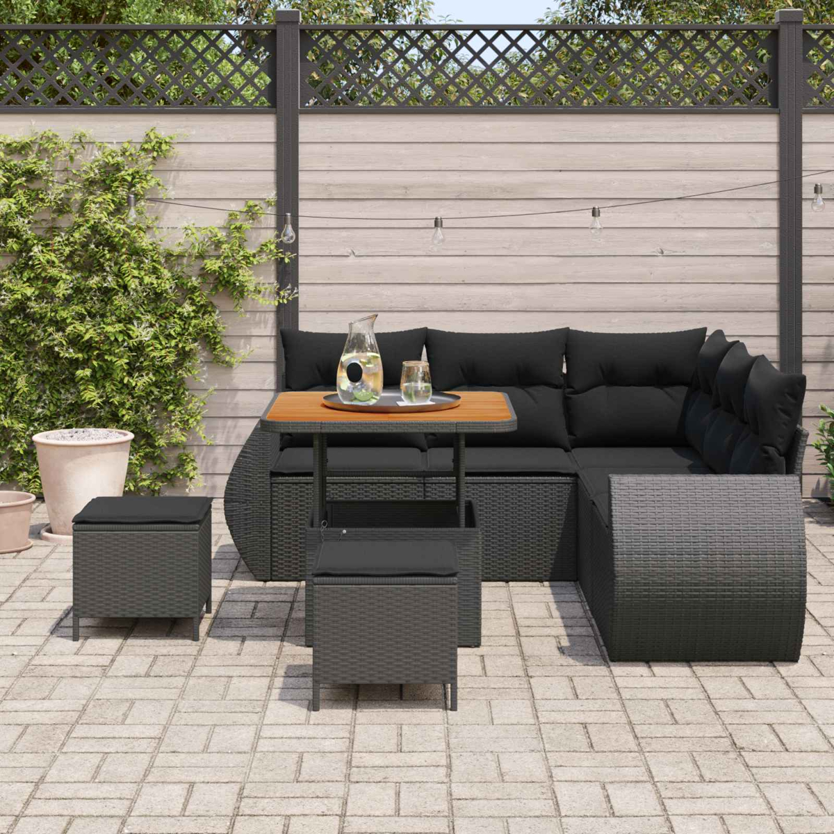 Ein dunkles Rattan-Sofa mit schwarzen Kissen und einem Tisch mit Getränken.