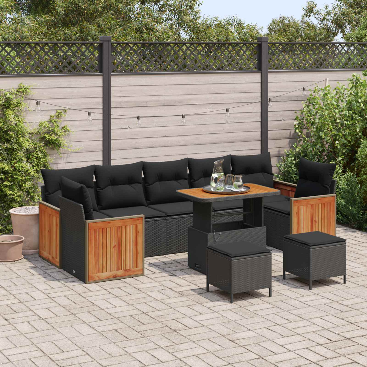Gartenlounge mit schwarzen Kissen und Holzakzenten auf Kopfsteinpflaster.