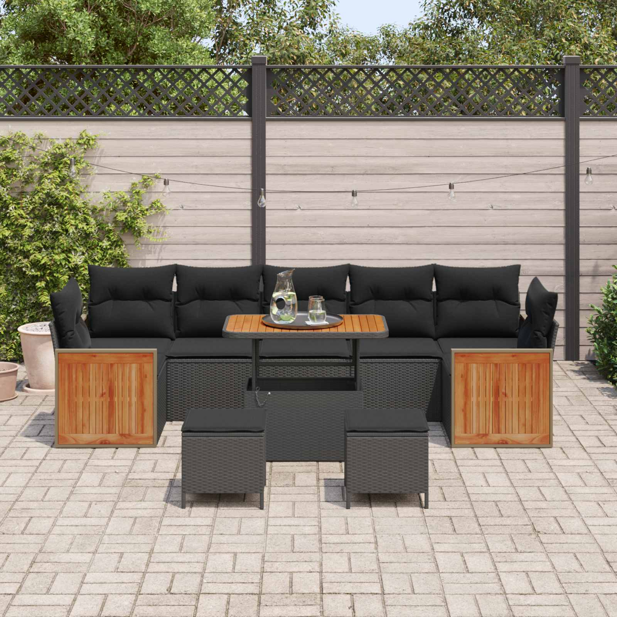 Ein dunkles Rattan-Sofa mit schwarzen Kissen und Holzakzenten auf einer gepflasterten Terrasse.