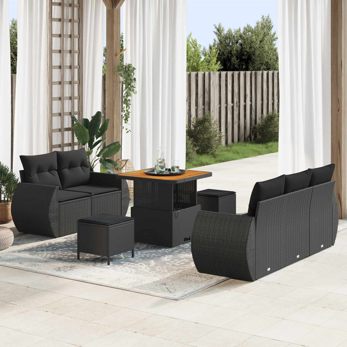 Ein schwarzes Rattan-Gartenmöbel-Set mit Sofa, Tisch und Hockern auf einer Terrasse.