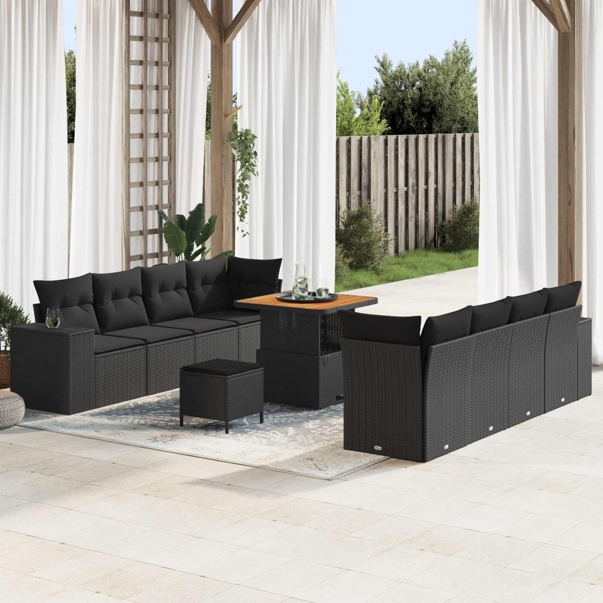 Ein schwarzes Rattan-Sofa mit Tisch und Hockern auf einer Terrasse.
