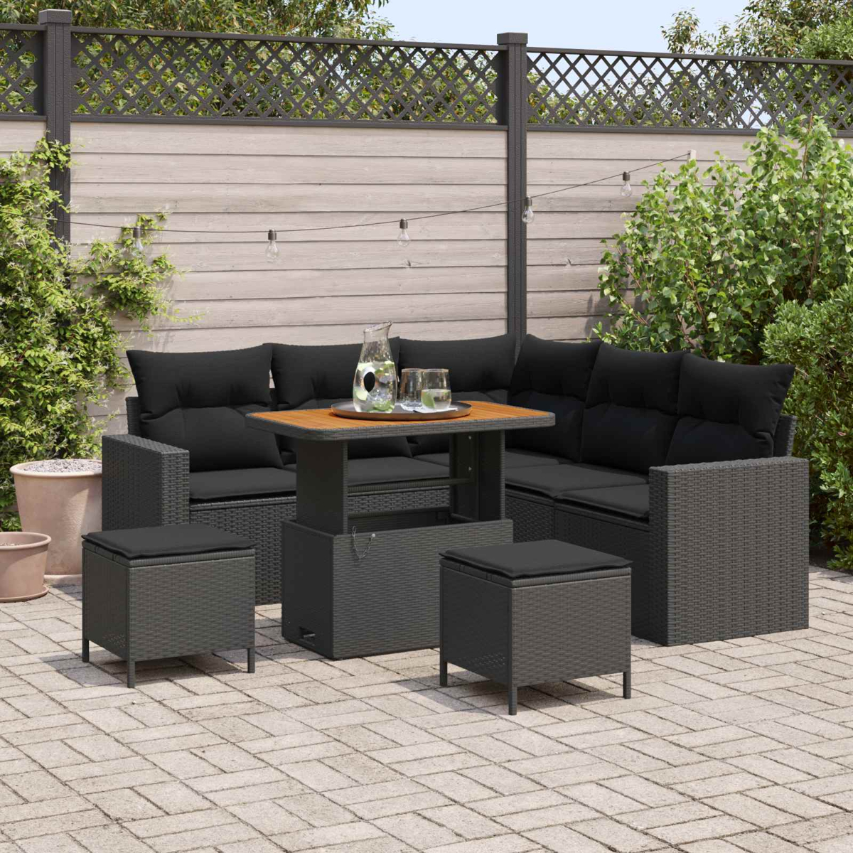 Dunkelgraue Rattan-Lounge-Garnitur mit schwarzem Tisch und Hockern auf einer Terrasse.