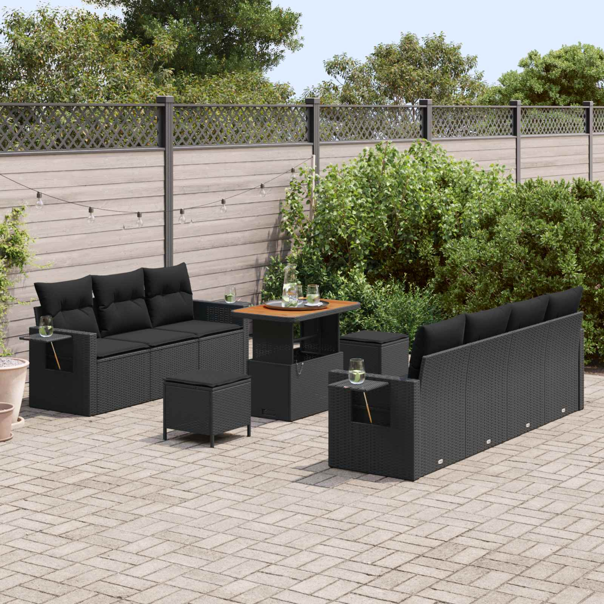 Draußenmöbel-Set aus schwarzem Rattan mit Sofas, Tisch und Hockern auf gepflastertem Hof.