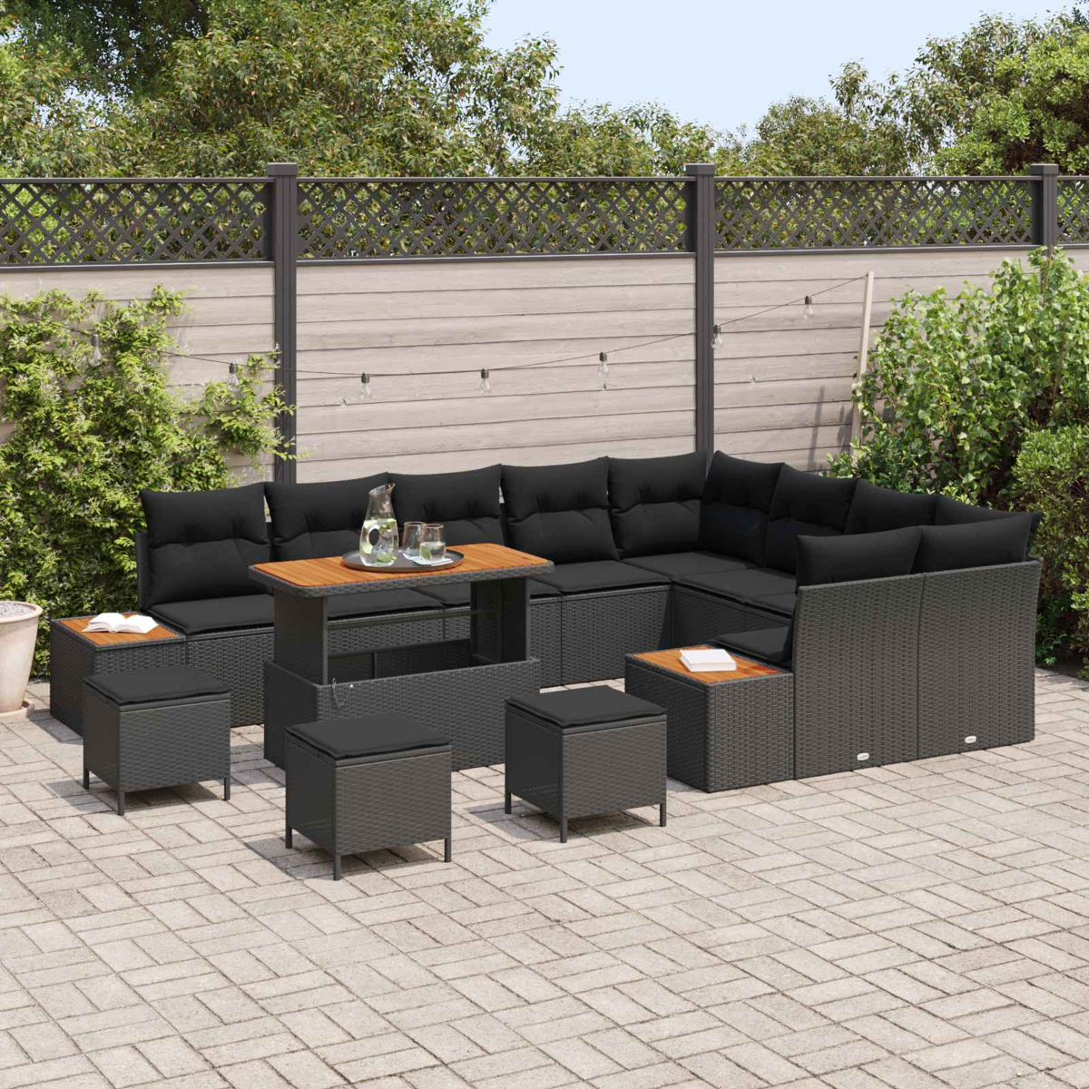 Dunkelgraue Gartenlounge-Möbel mit schwarzen Kissen auf einer gepflasterten Terrasse.