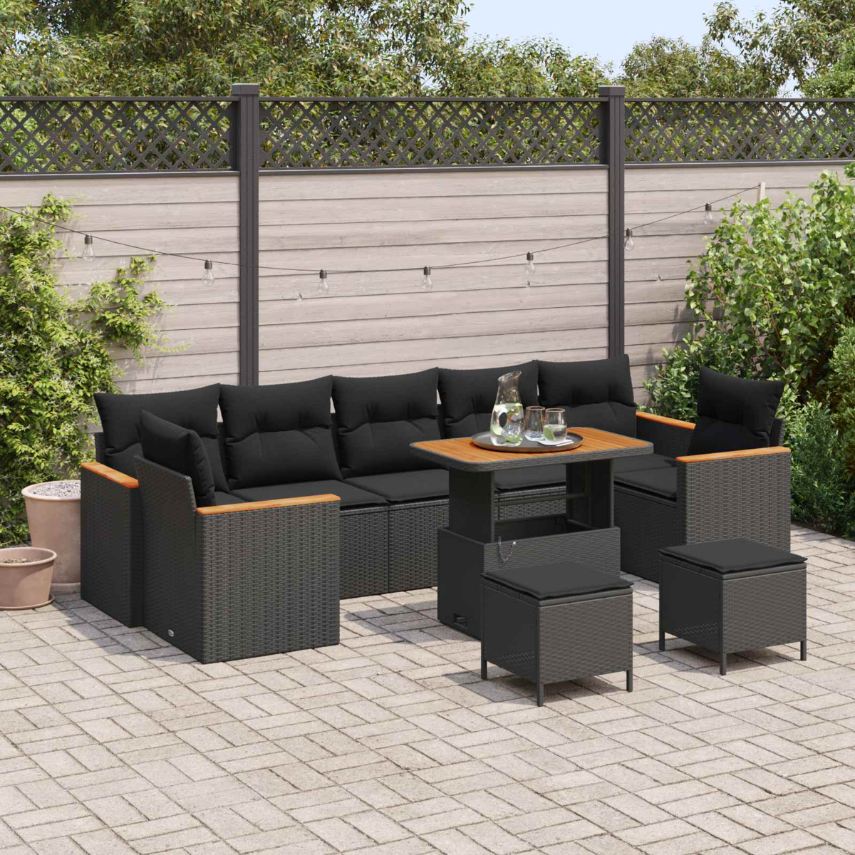 Ein dunkles Lounge-Set mit schwarzen Kissen auf einer Steinterrasse, umgeben von Grün.