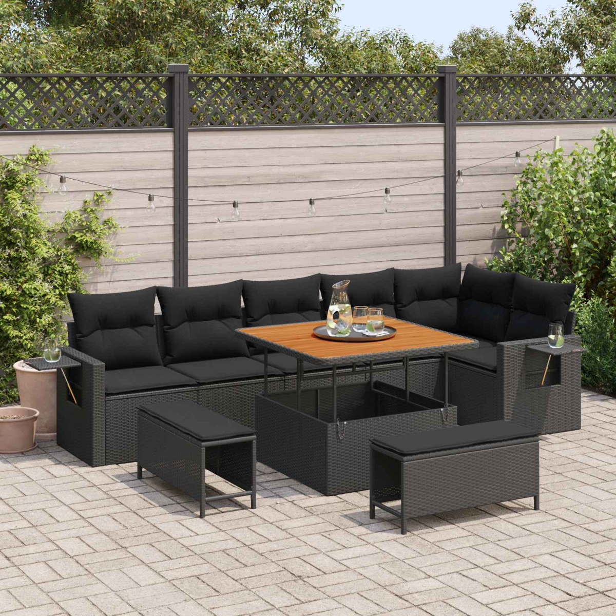 Gartenlounge mit schwarzem Geflecht und Auflagen, Holztisch, Bänken.