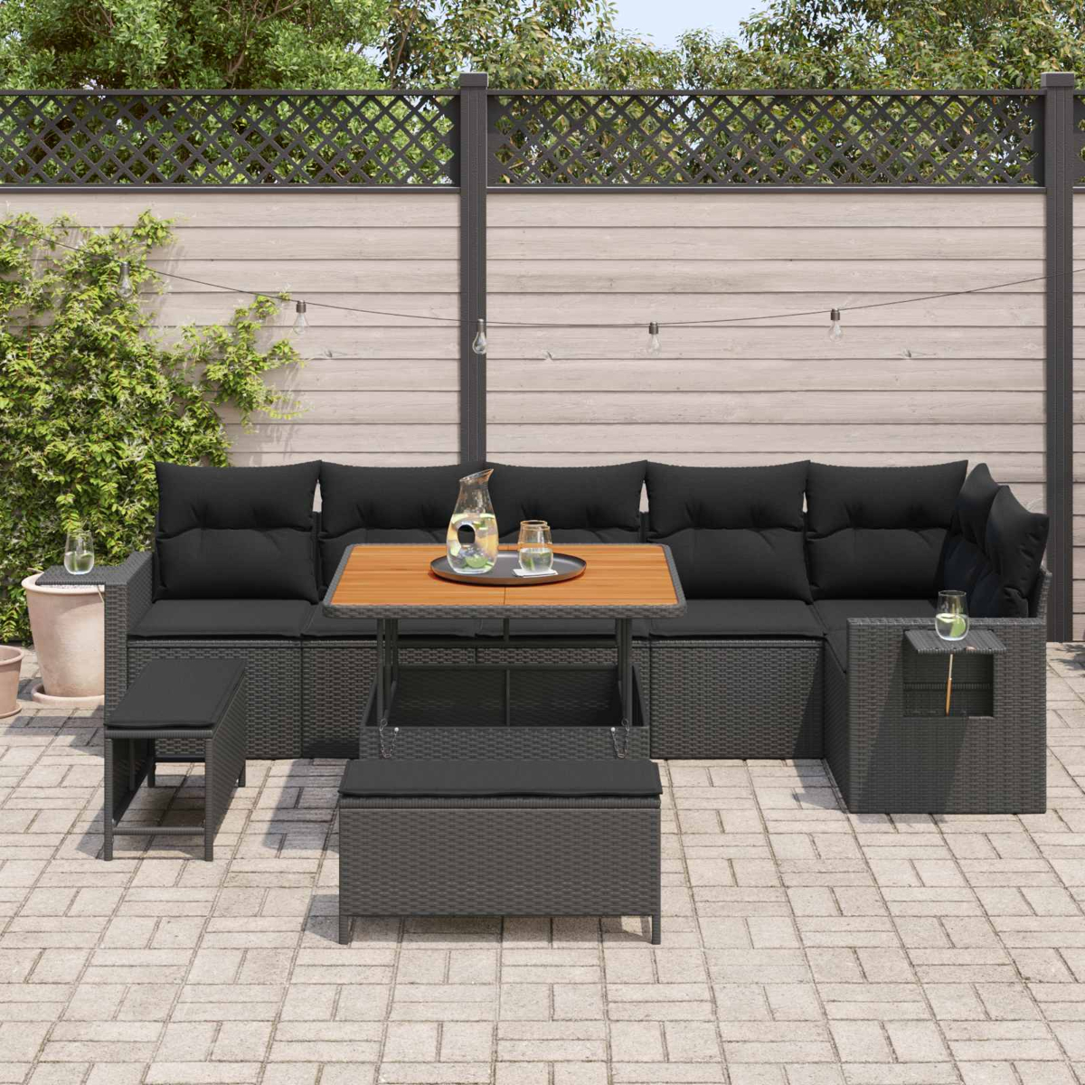 Dunkelgraue Rattan-Lounge-Möbel mit schwarzen Kissen auf einer gepflasterten Terrasse.