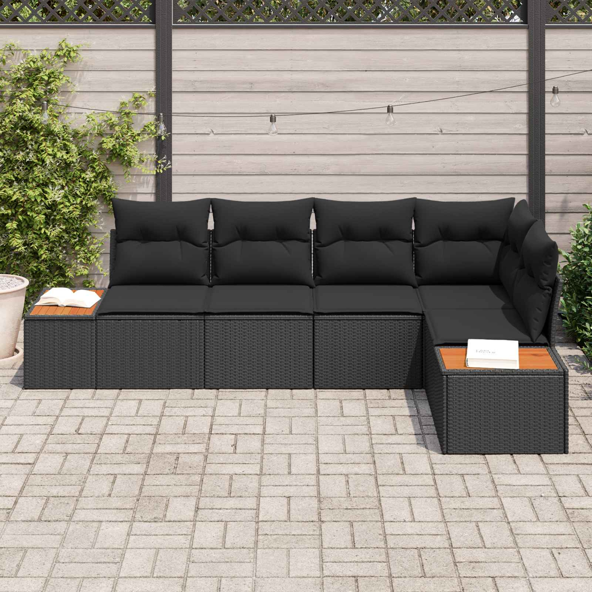 Ein schwarzes Lounge-Set mit Kissen auf einer gepflasterten Terrasse, mit Lichtern.