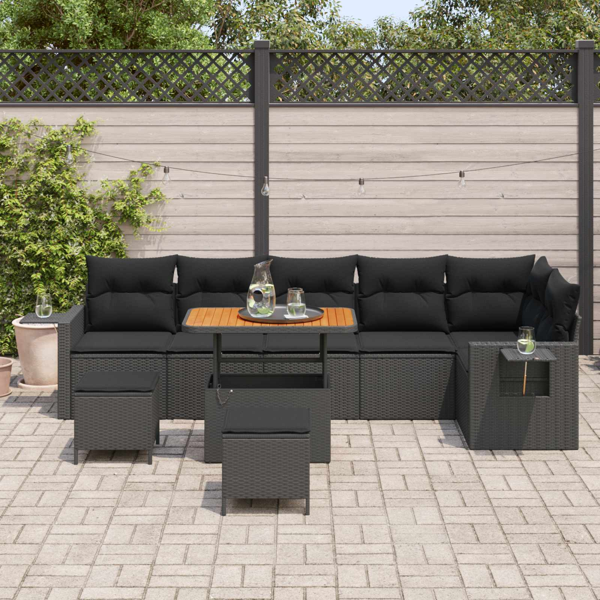 Dunkelgraues Rattan-Lounge-Set mit Kissen, Holztisch, Gläsern und Dekoration auf einer Steinterrasse.