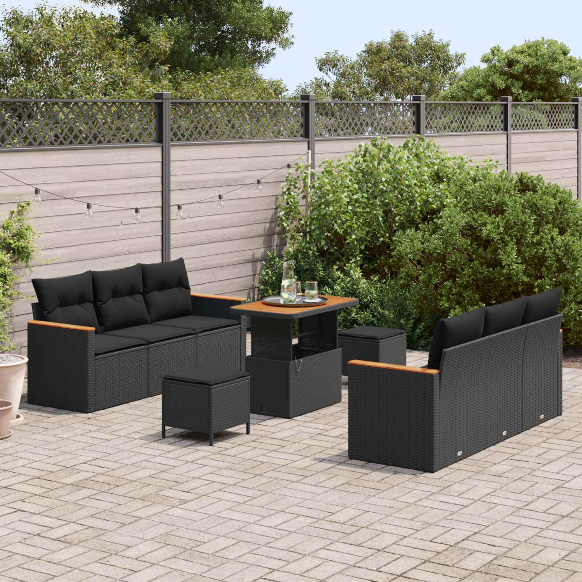 Schwarzes Gartenmöbel-Set auf einer Terrasse mit Holzzaun und Lichtern.
