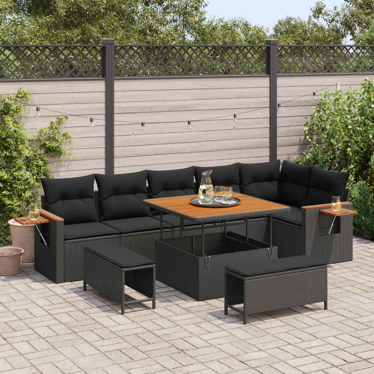Gartenmöbel-Set mit schwarzen Kissen, Holztisch und Lichterkette.