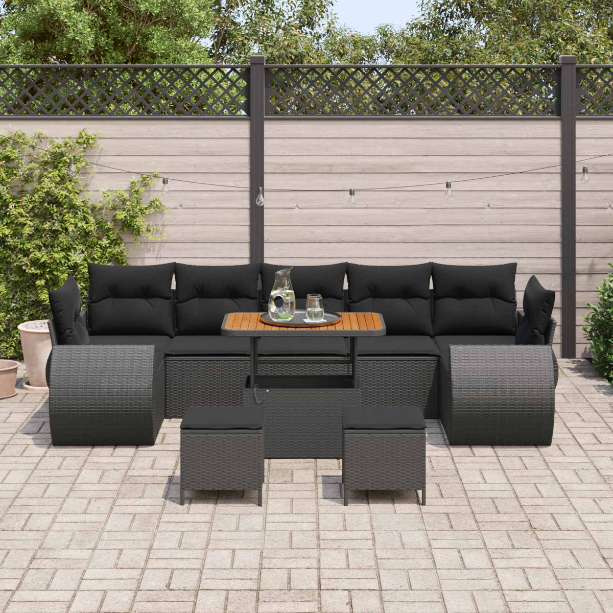 Outdoor-Rattansofa mit schwarzen Kissen, Couchtisch und Hockern auf einer Terrasse.