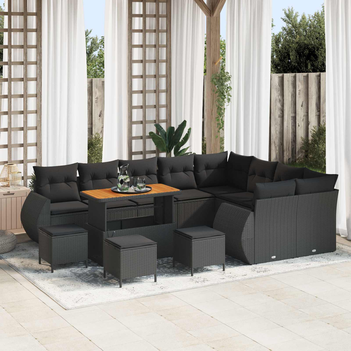 Dunkelgraue Rattan-Lounge mit Holztisch und Hockern auf einer Veranda.