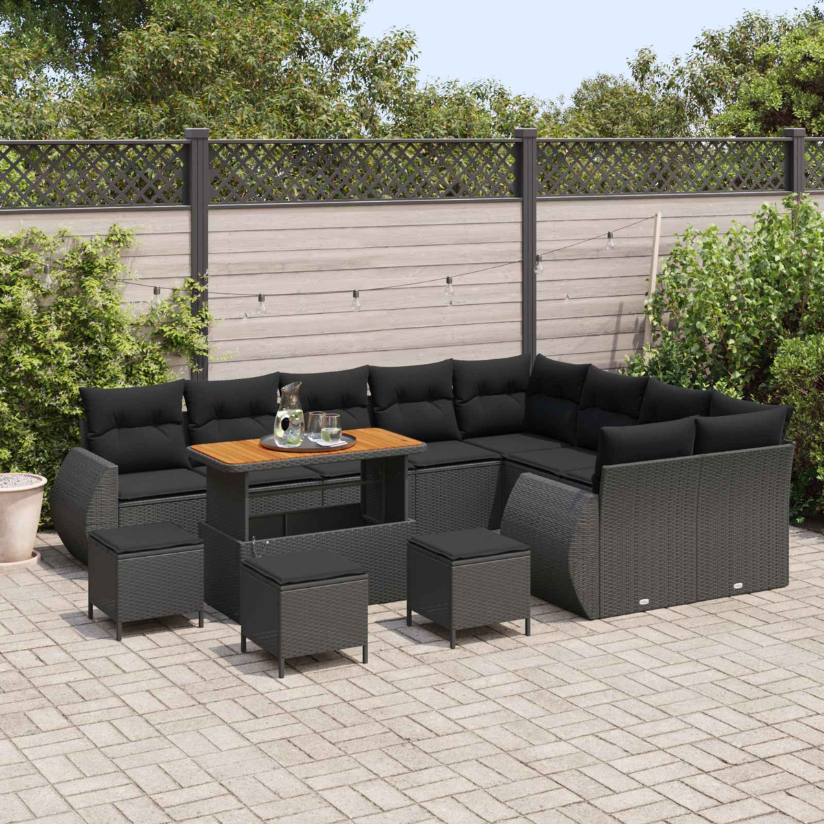 Dunkle Polstermöbel mit Tisch und Hockern auf einer gepflasterten Terrasse.