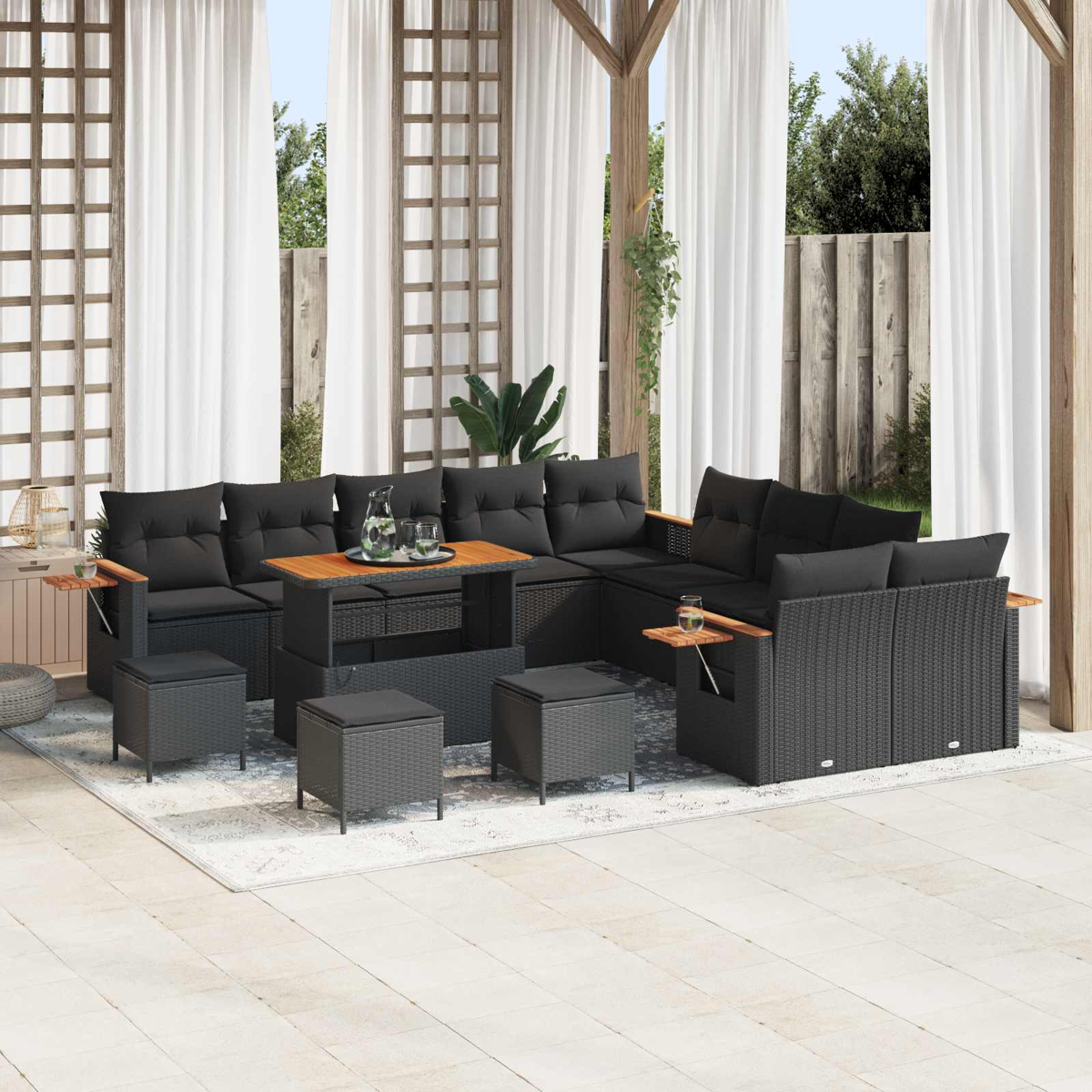 Mobili lounge in rattan grigio scuro con cuscini neri sotto un pergolato con tende bianche.