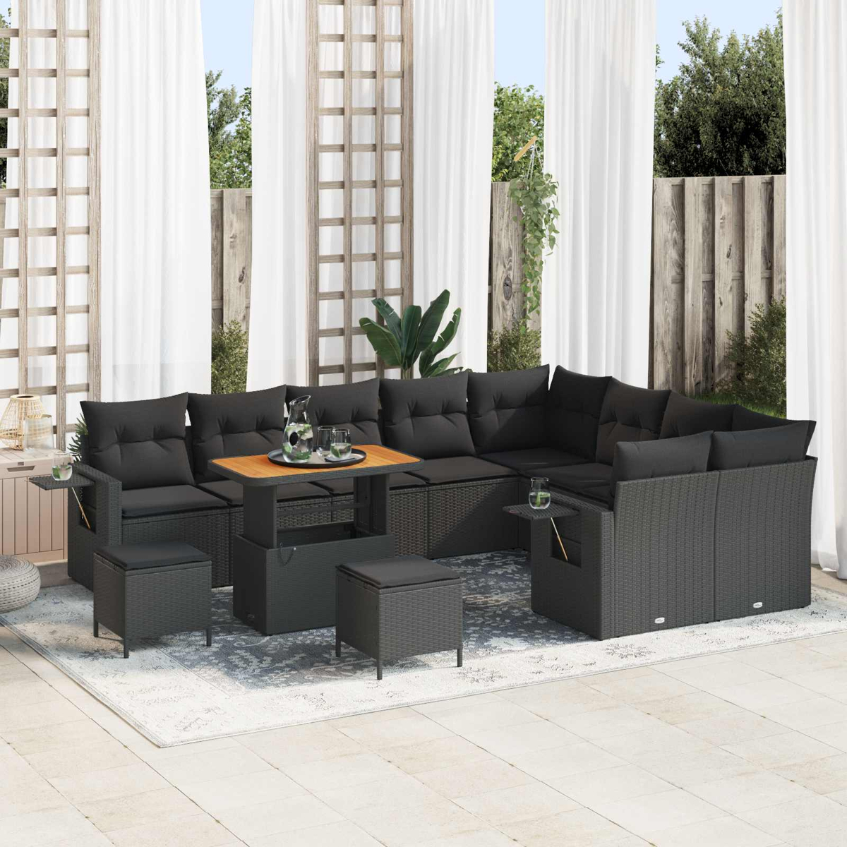 Dunkelgraues Rattan-Sofa mit Kissen, verstellbarem Tisch und Hockern auf einer Terrasse.