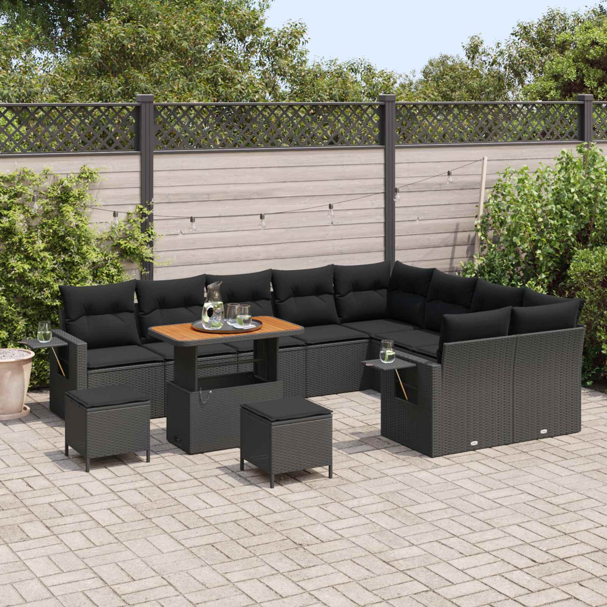 Dunkles Rattan-Sitzmöbel-Set mit schwarzen Kissen auf einer Steinterrasse.