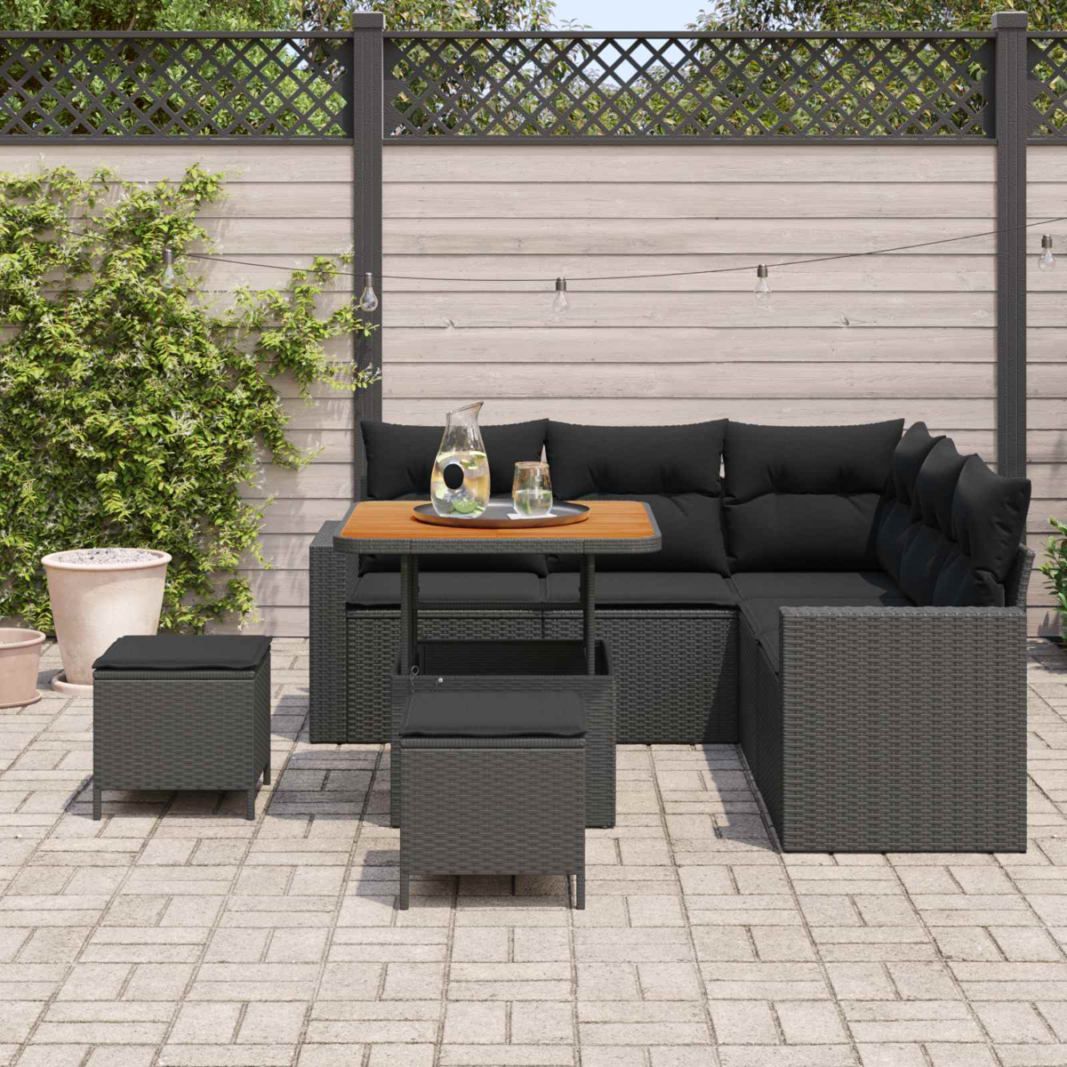Dunkelgraue Rattan-Lounge-Möbel mit schwarzen Kissen auf einer gepflasterten Terrasse.