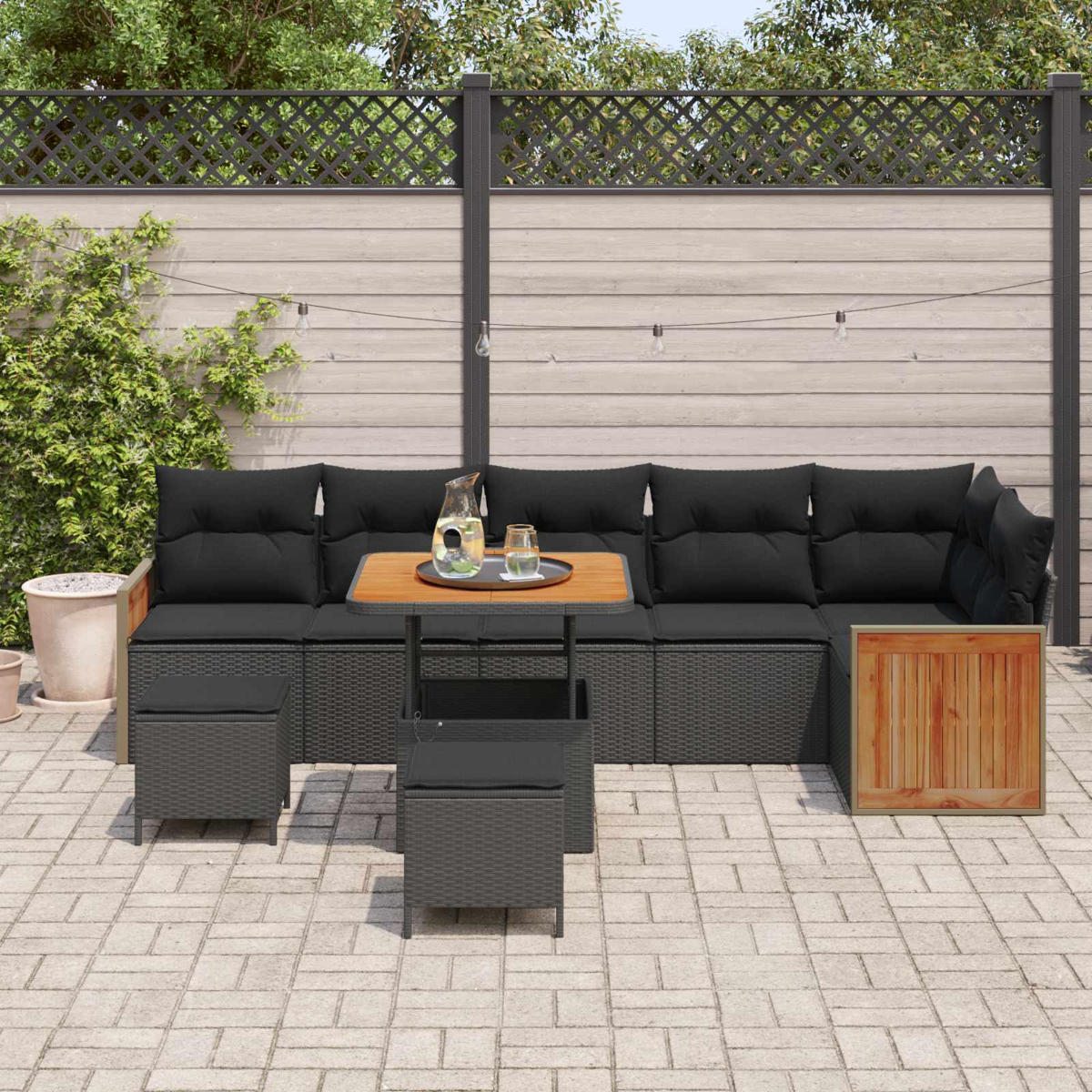 Mobiliario de salón gris oscuro con cojines negros, mesa de madera, jarra y vasos.