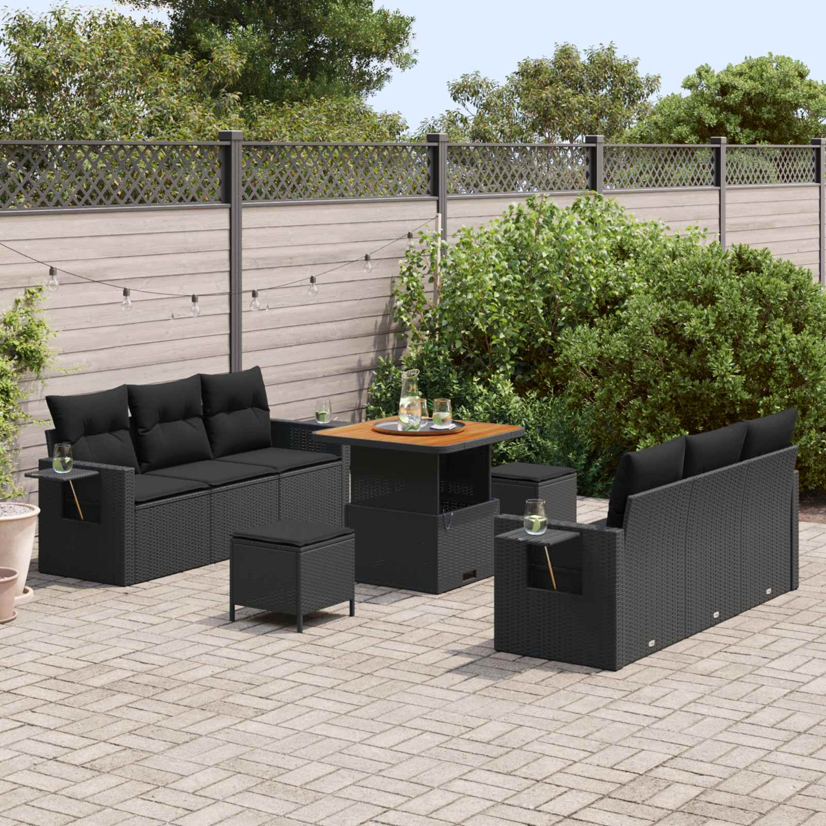 Gartenlounge mit schwarzen Kissen, Feuerstelle und Glaswaren auf einer gepflasterten Terrasse.