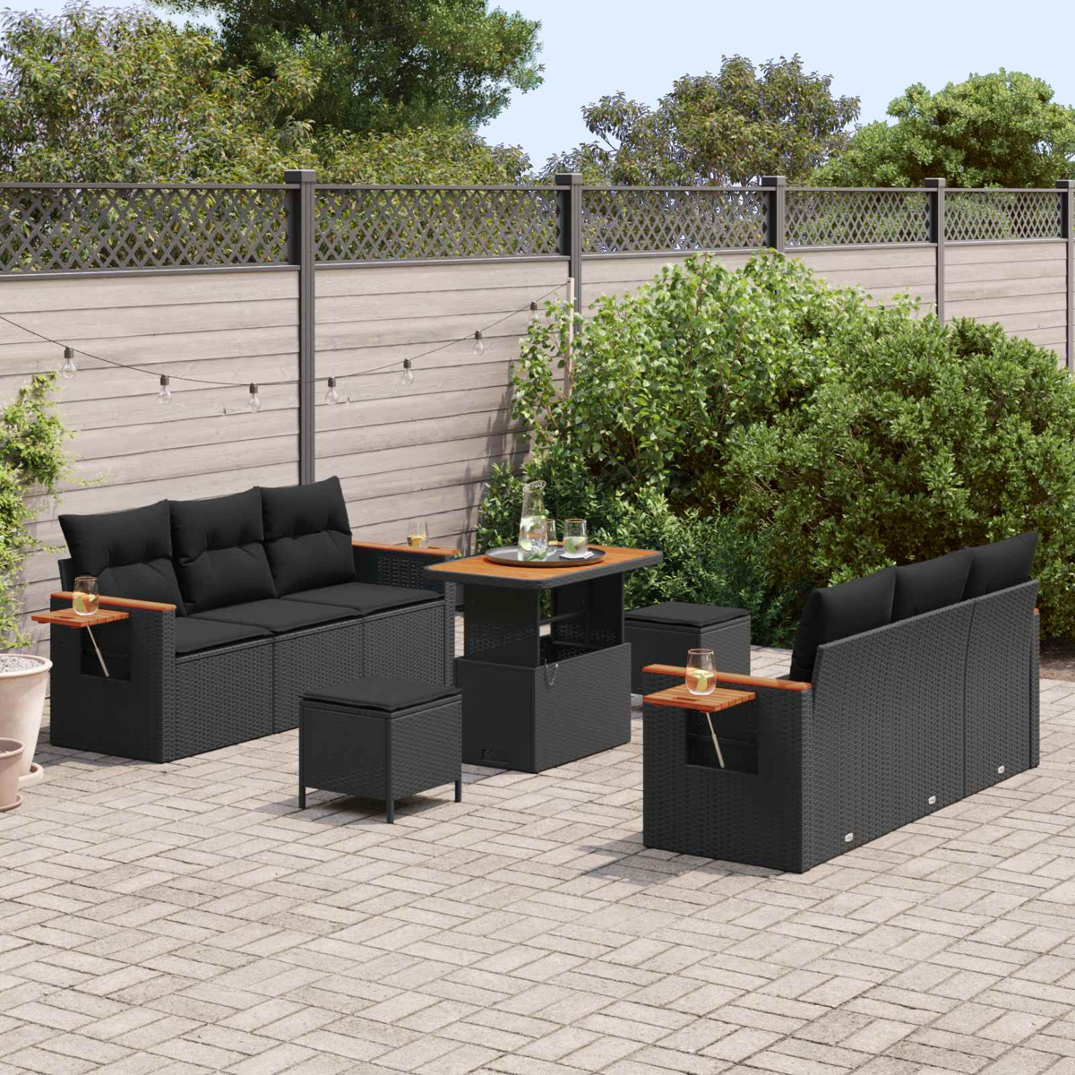 Schwarzes Rattan-Gartenmöbel-Set auf einer Steinpatio mit Bäumen im Hintergrund.