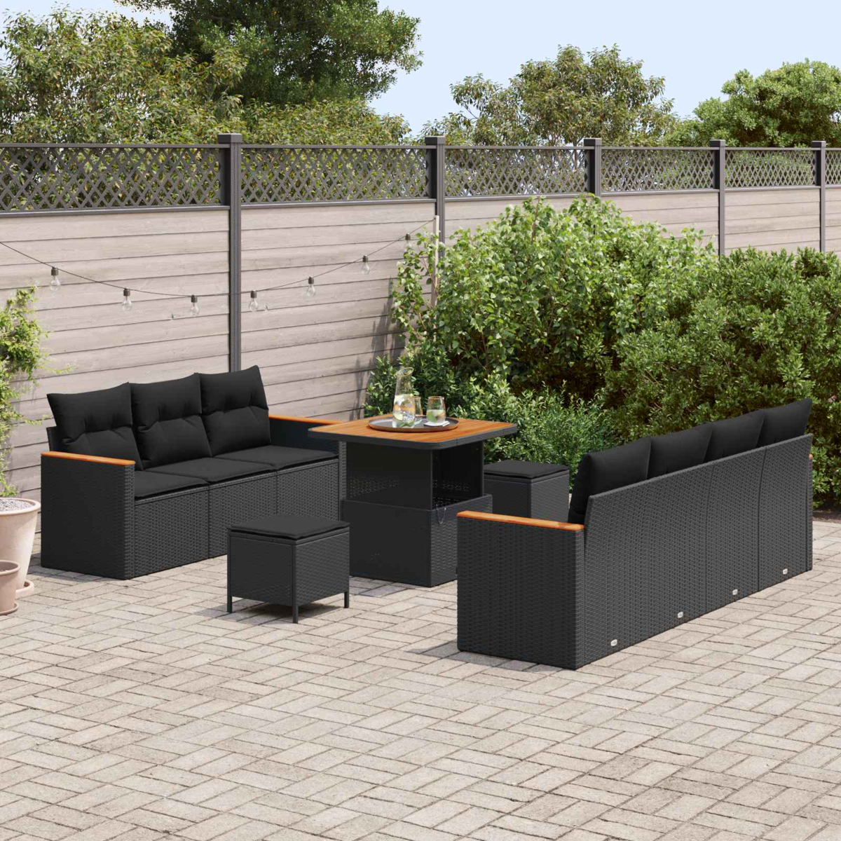 Gartenlounge mit schwarzen Polstern, Tisch und Hockern auf Kopfsteinpflaster.