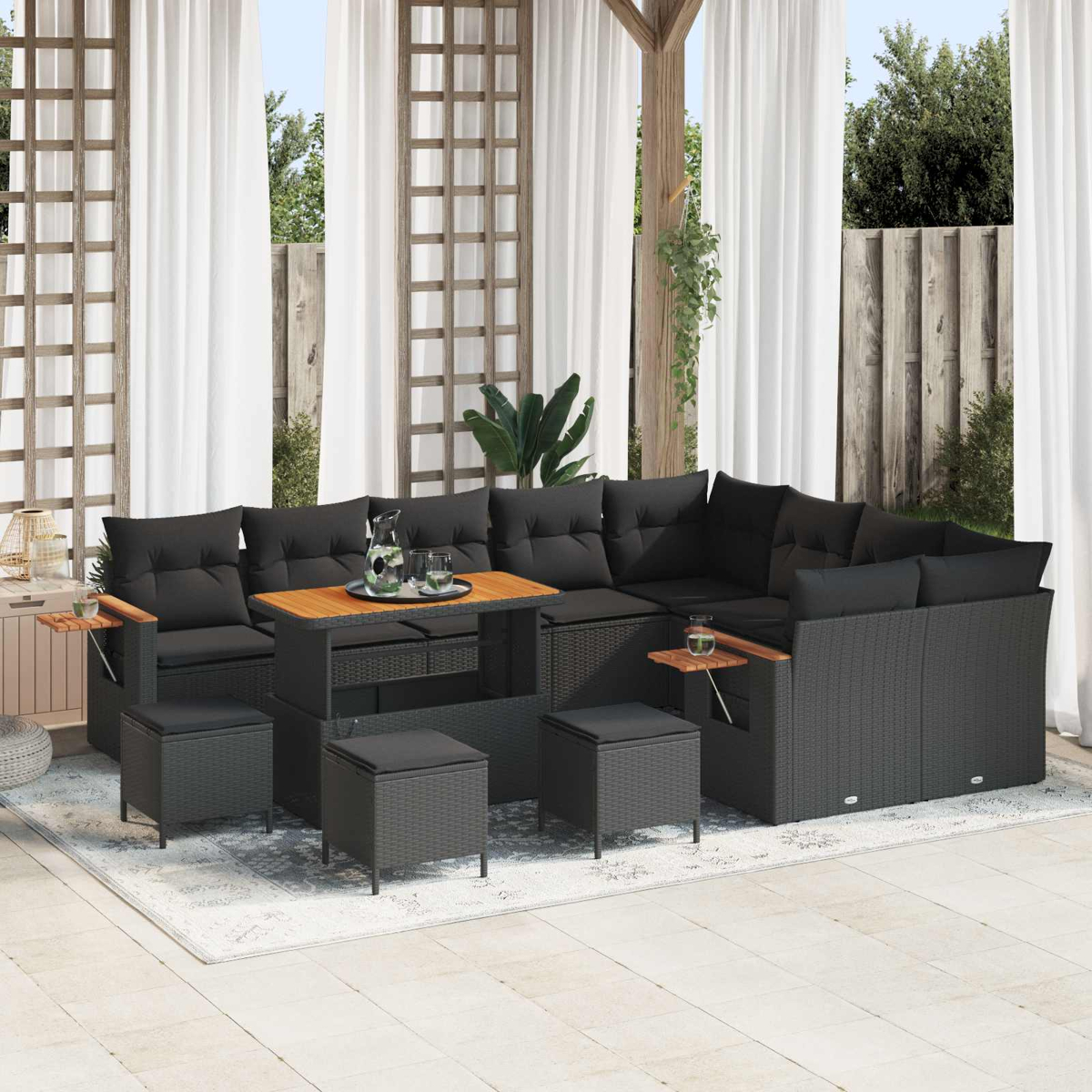 Ein dunkles Rattan-Lounge-Set mit schwarzen Kissen steht auf einer Veranda.