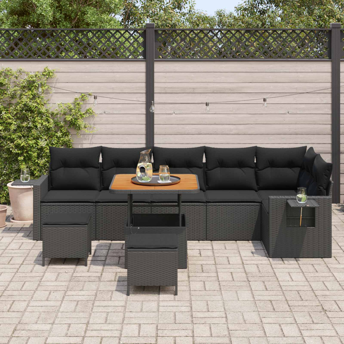 Dunkelgraue Rattan-Lounge-Garnitur mit schwarzen Kissen auf einer Steinterrasse.