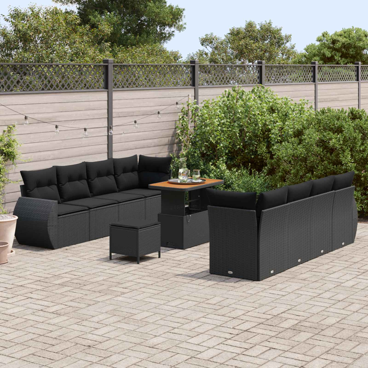 Gartenlounge mit schwarzen Kissen und einem verstellbaren Tisch auf einem Steinpflaster.