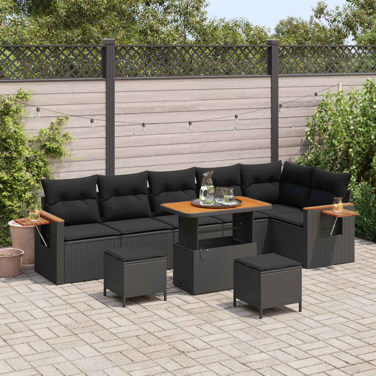 Dunkle Gartenmöbel mit schwarzem Sofa, Hocker und Tisch auf einer Terrasse.