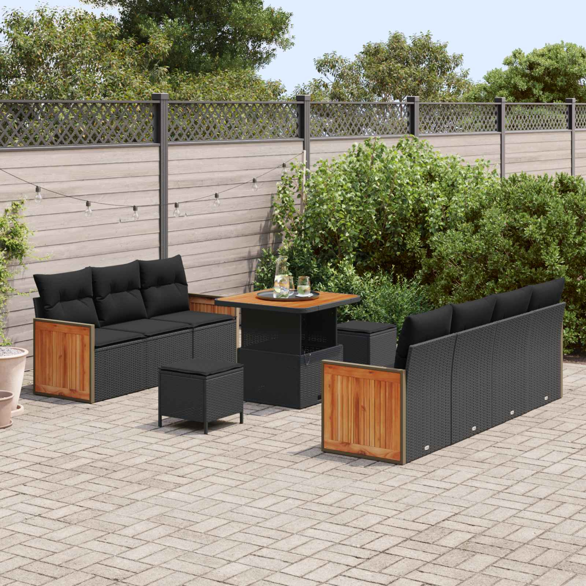 Gartenlounge mit schwarzen Sofas, Hockern und einem Tisch auf einer Pflasterterrasse.