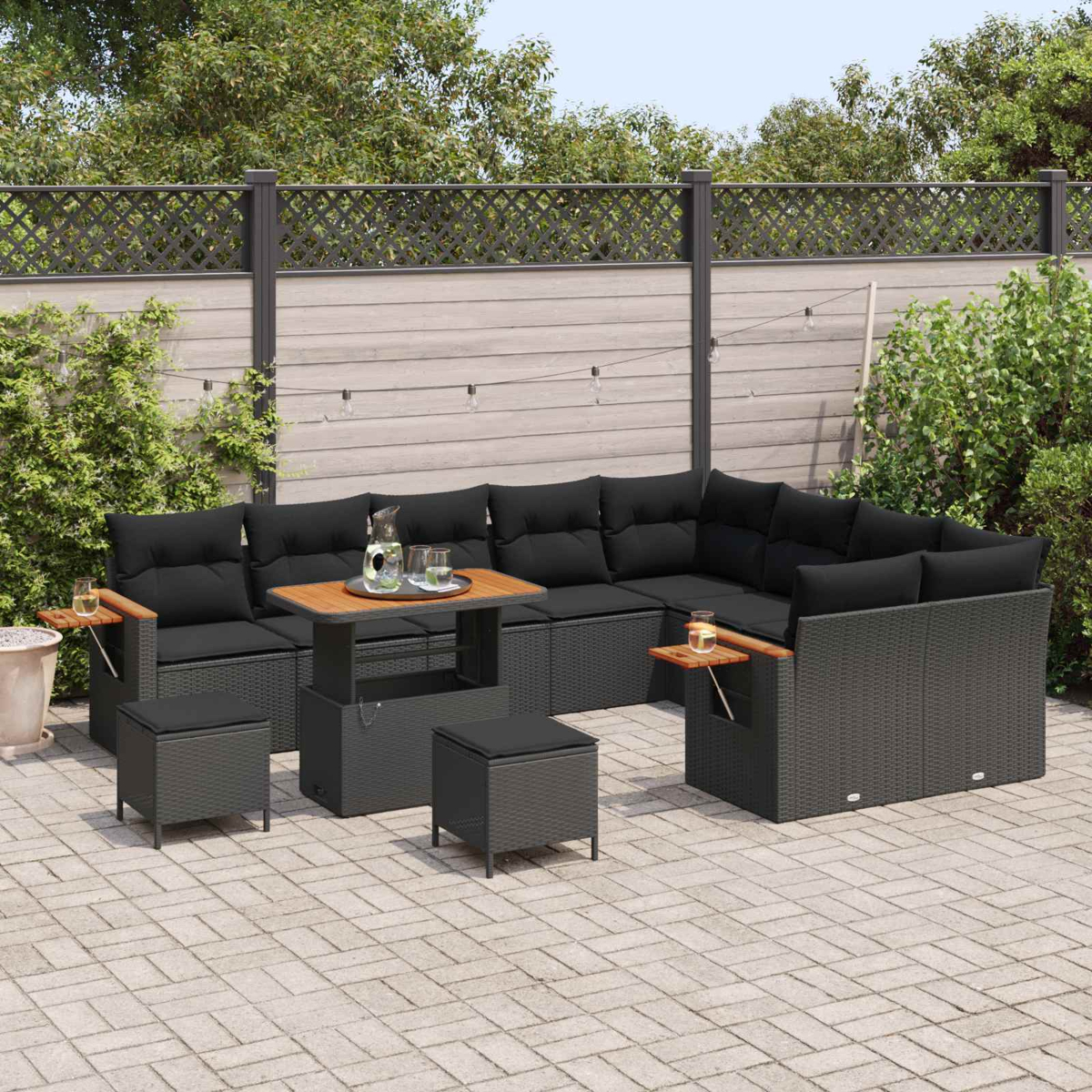 Ein dunkles Lounge-Set aus Rattan mit schwarzen Kissen auf einer Steinterrasse.