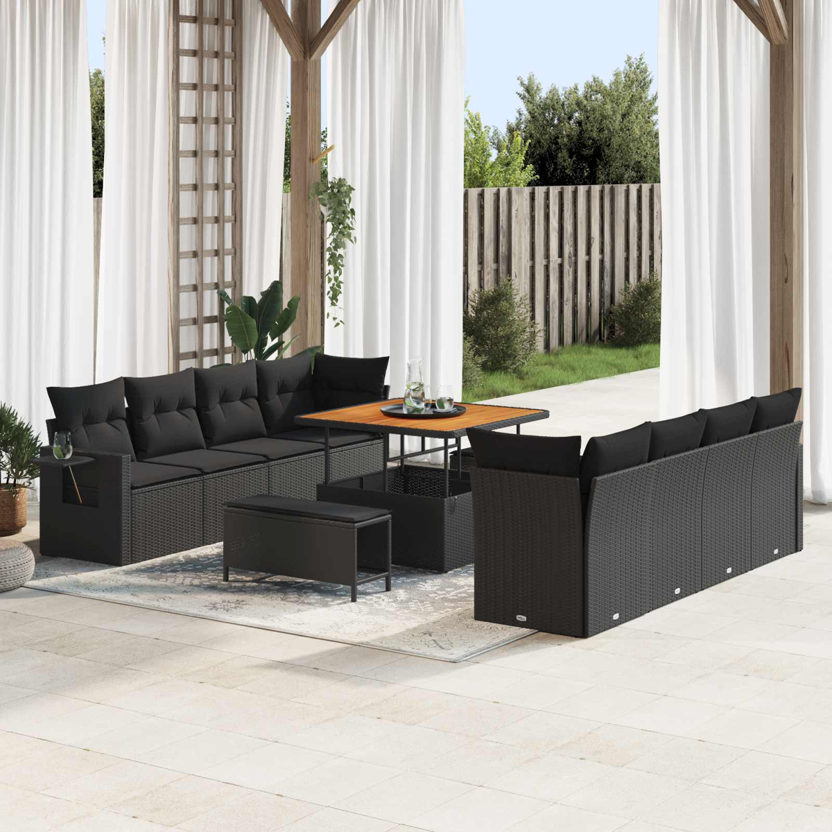 Set di sedute in rattan nero con tavolo su patio, tende bianche sullo sfondo.