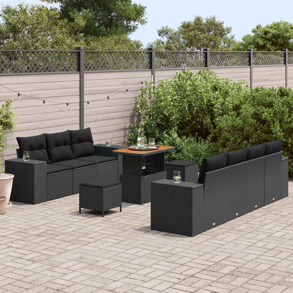 Draußenmöbel: schwarzes Rattan-Sofa, Tisch, Hocker auf gepflasterter Terrasse.